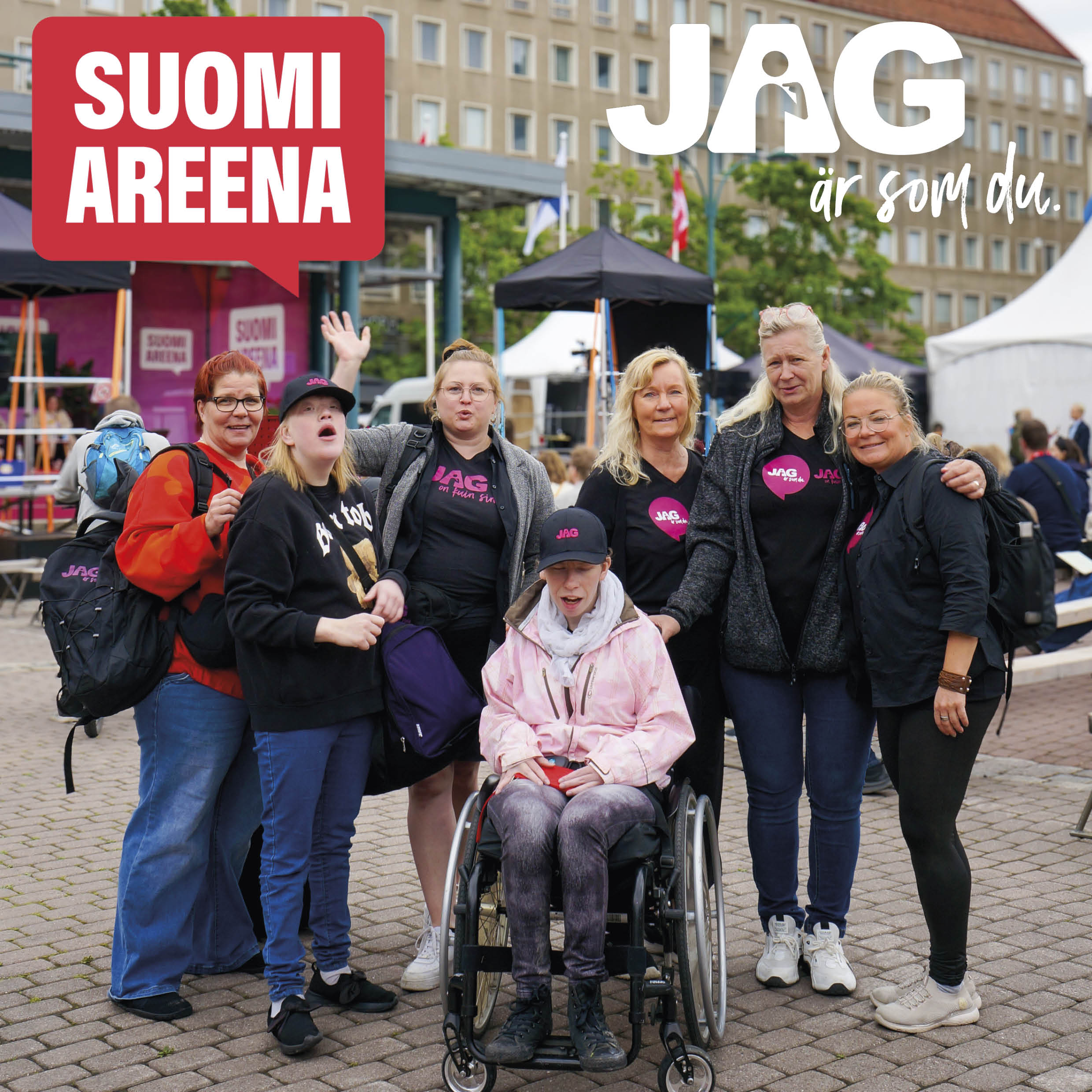 Seitsemän iloista eri-ikäistä naista, joista yksi on pyörätuolissa, taustalla lava ja yleisö. Suomiareena- ja JAG-logot näkyvissä.