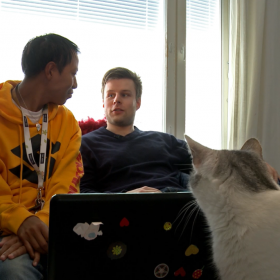 En kille med assistent samt en katt framför datorn
